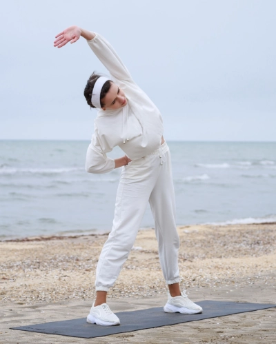 Pige klaedt i zenith der laver yoga paa en strand