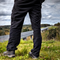 Person i hurtigtoerrende vandrebukser staar paa groent underlag med landskab i baggrunden