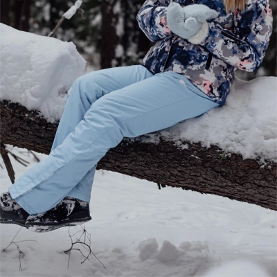 Person i lysebla ekspeditions vinterbukser sidder paa sne daekket traestamme