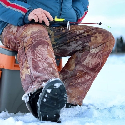 Person i isolerende gletsjer bukser sidder paa orange kasse i sneen