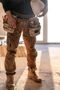 Person i slidstaerke arbejdsbukser med vaerktoejsbaelte holder hjelm