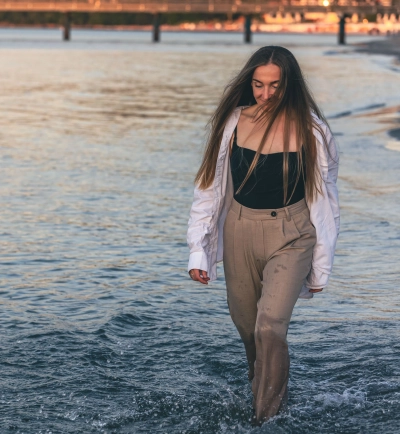 Kvinde i vandtaette stroembukser gaar i vandkanten ved solnedgang