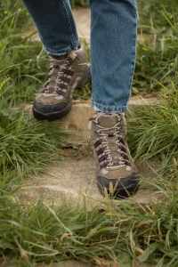 Person i vandrestovler og jeans gaar paa sti med graes