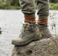 Person i vandrestoevler staar paa sten ved vand