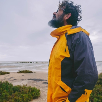 Mand med skaeg i gul og morkeblaa kystnaer komfort jakke kigger op mod himlen ved kysten