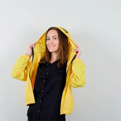 Kvinde i gul bjergkam vindjakke med haetten oppe smiler