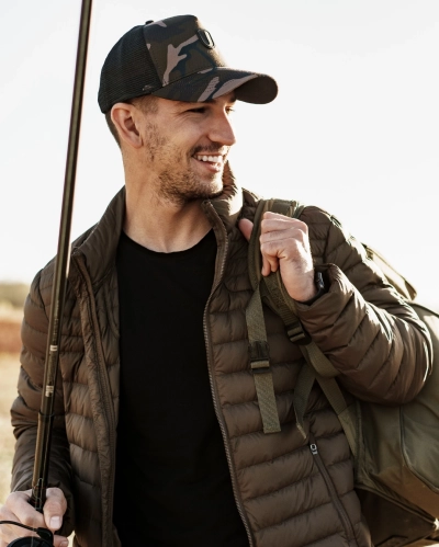 Mand i brun globetrotter rejsejakke med kasket, rygsaek og fiskestang