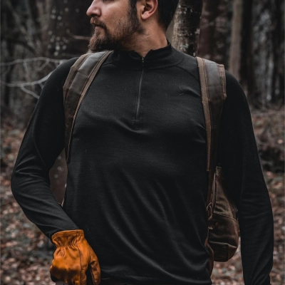 Mand med skaeg i sort taktisk merino troeje og ryksaek i naturen