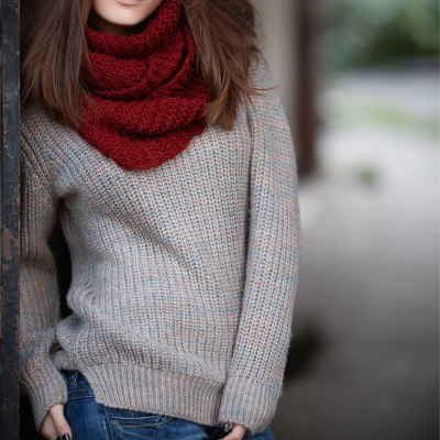 Kvinde i stjernekigger uldtroeje og roedt halstørklaede laener sig op ad vaeg