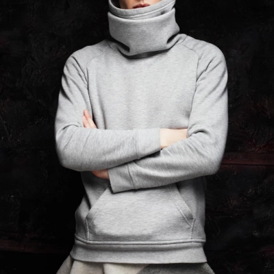 Person i graa haettetroie med hoej hals staar med krydsede arme
