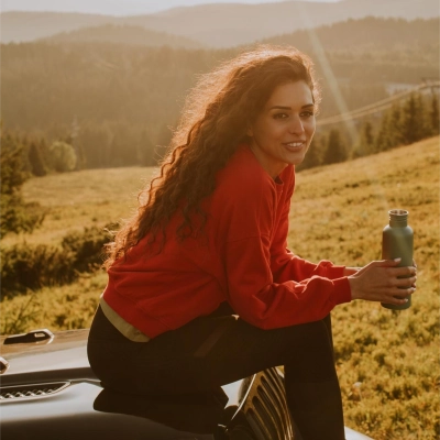 Kvinde med langt, kroellet, brunt haar, sidder med Flux Terra Troeje i naturlandskab