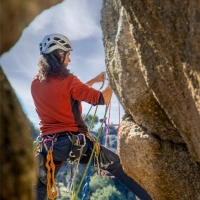 Kvinde med hjelm klatrer op ad en klippe med reb og udstyr