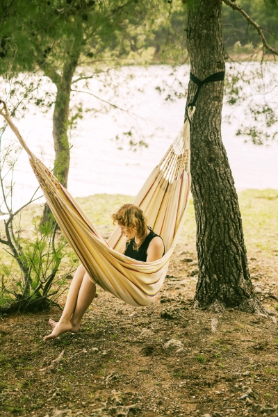 Kvinde sidder i haengekoeje med myggenet ved flodbred